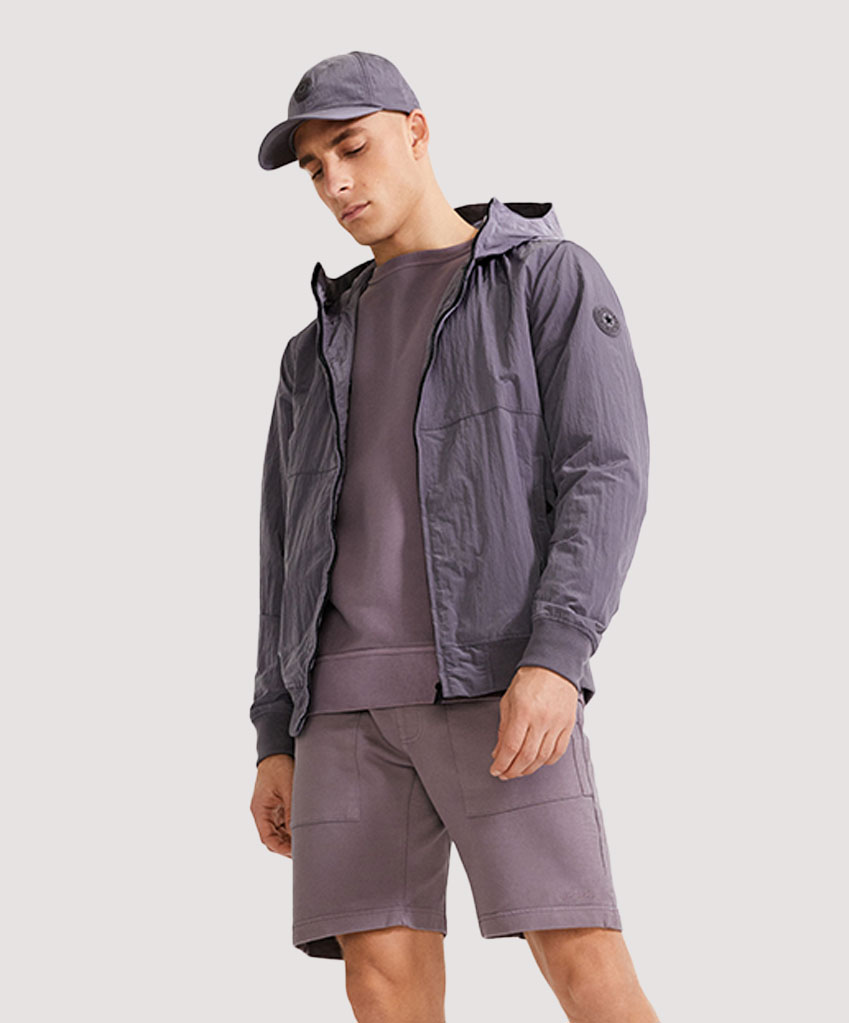 Een model draagt een softshell jas in de kleur shark. Verder draagt het model een airforce pet, sweater en shorts in de kleur shark.