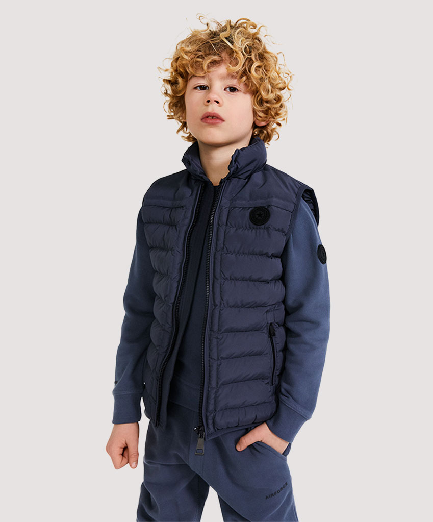 Een kind draagt een airforce bodywarmer, een sweater en shorts in de kleur ombre blue.
